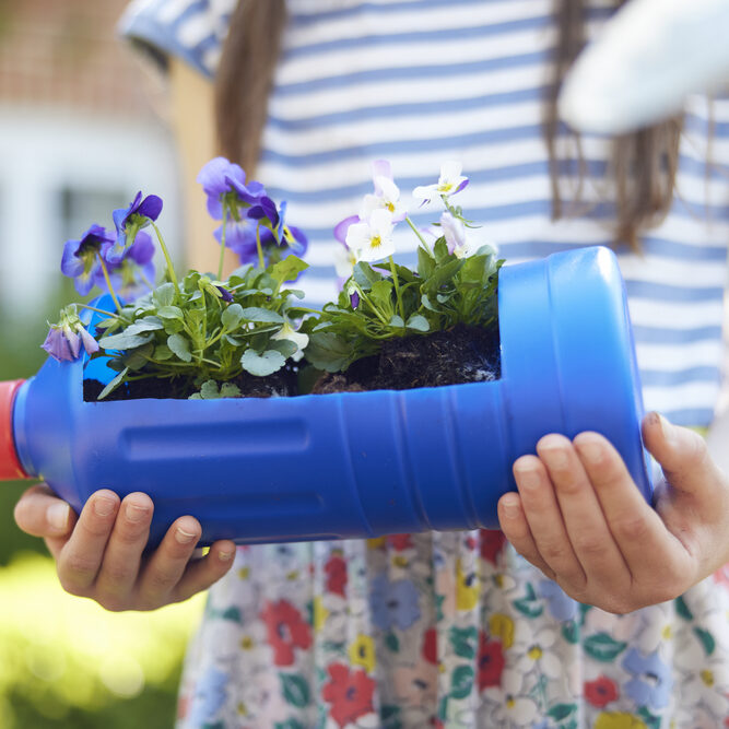 Close Up Of Girl Holding Recycled Plant Holder From Plastic Bottle Packaging Waste In Garden At Home